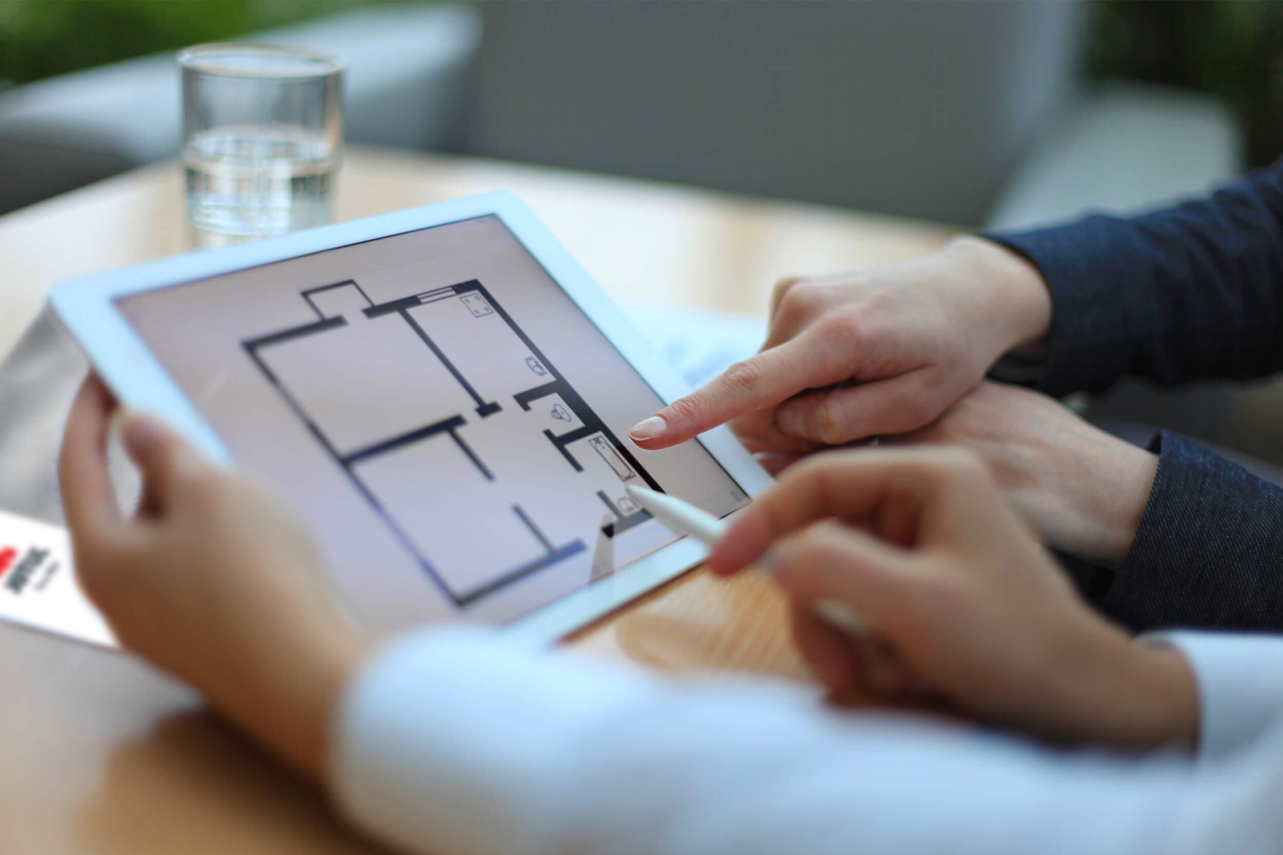 Handen wijzend op iPad met een vel kamerverdeling in een huis.