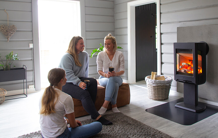 Drie meisjes zittend op een bruine poef in een grijze woonkamer voor de Jøtul F 167 houtkachel